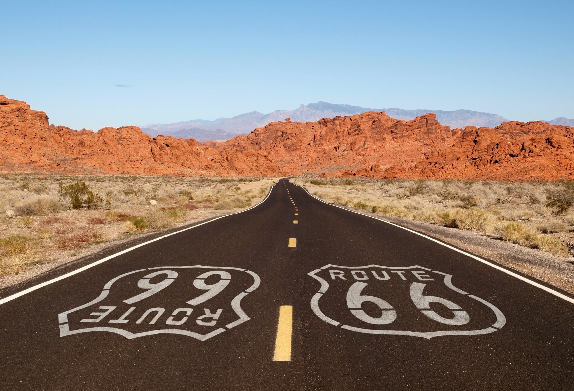 Route 66 pavement sign with Mojave desert red rock mountains_shutterstock_121945762-1 Route 66 pavement sign with Mojave desert red rock mountains_shutterstock_121945762-1
